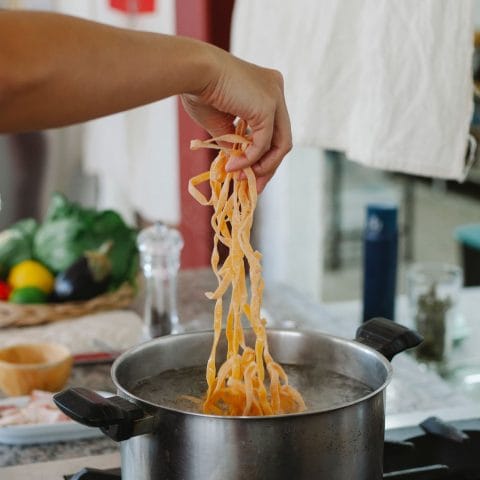Hand die pasta in een pan met kokend water doet, het moment waarop je de hoeveelheid per persoon afmeet