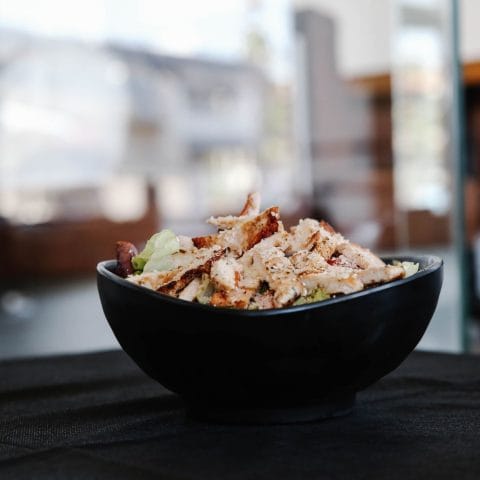 Salade met gegrilde kip en groente in een zwarte kom, een eiwitrijke lunch