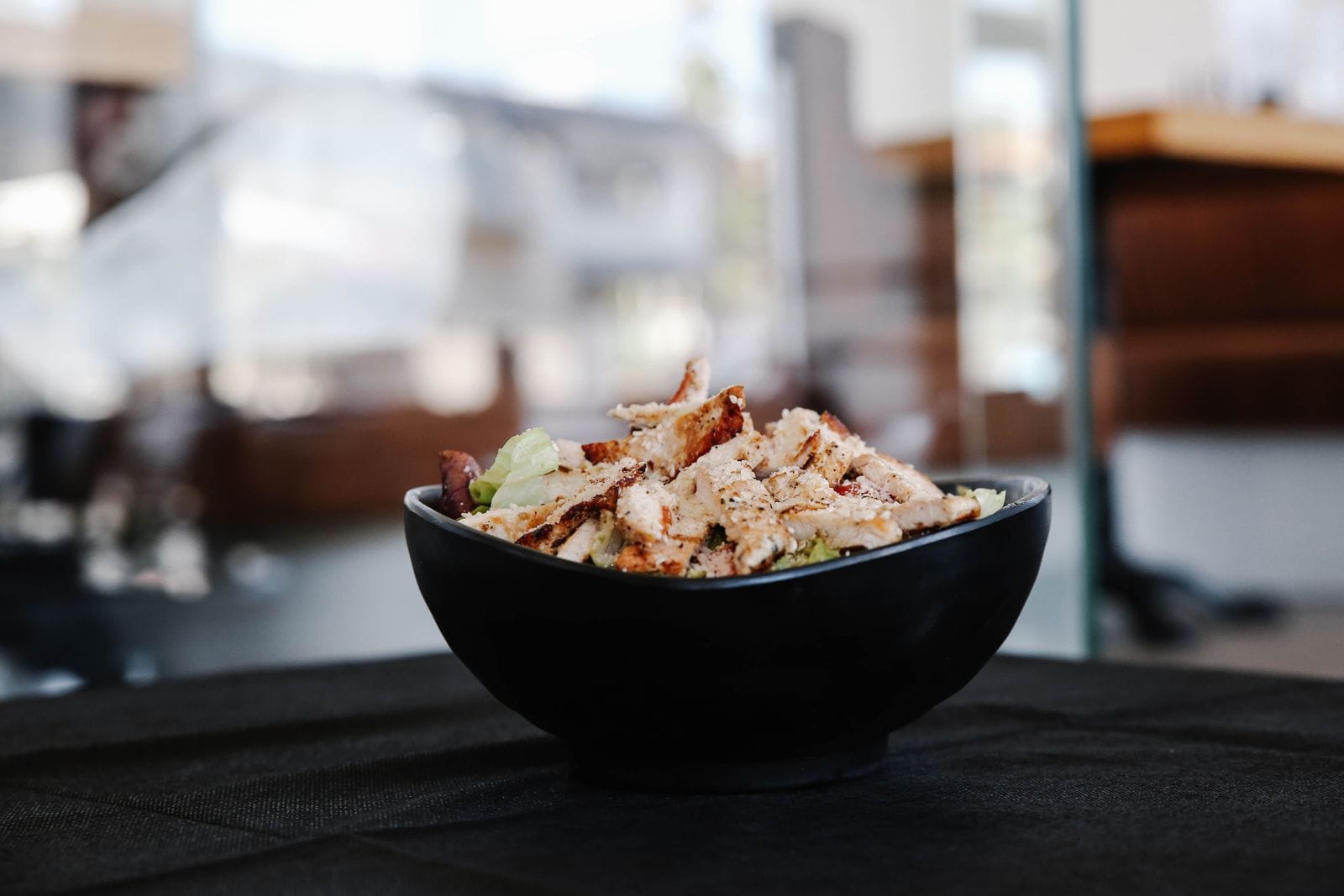 Salade met gegrilde kip en groente in een zwarte kom, een eiwitrijke lunch
