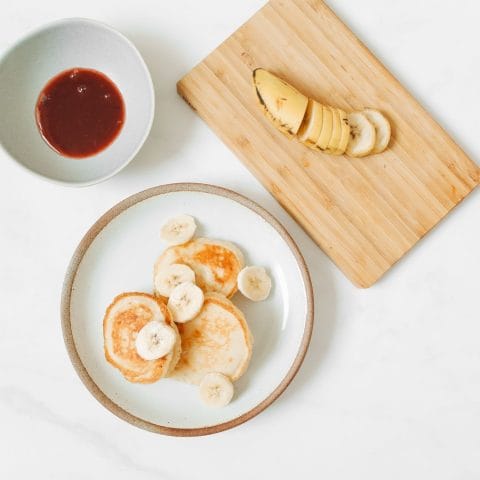 Stapeltje pannenkoekjes met plakjes banaan op een ontbijtbord in het ochtendlicht